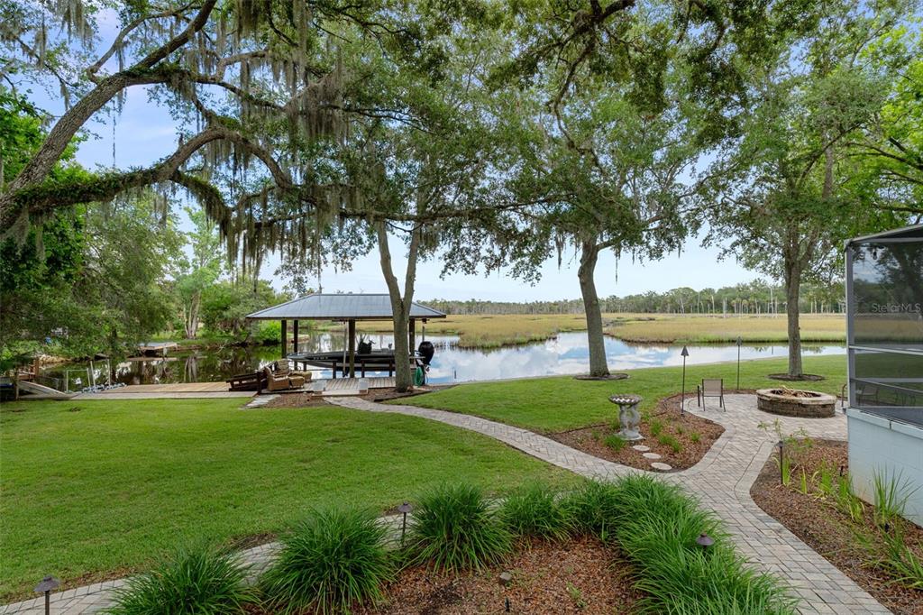 A backyard features a stone patio, a boat dock, and a view of a marshy waterway — 6085 S ROYAL DRIVE, HOMOSASSA, FL