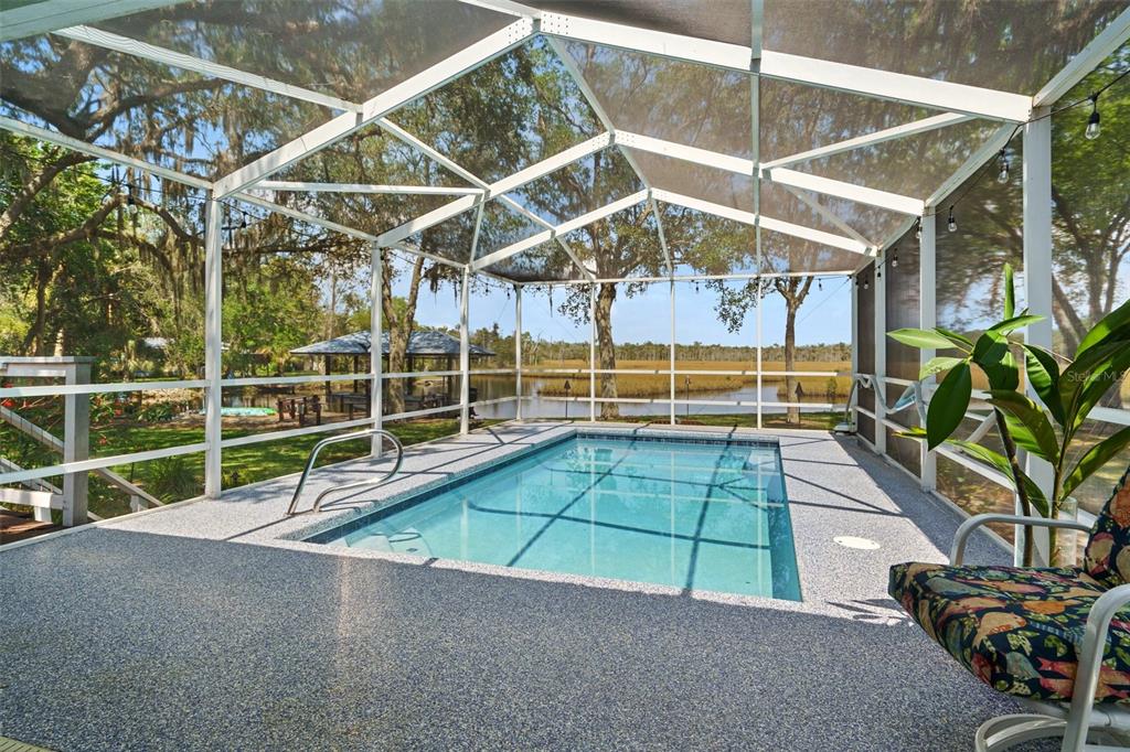 A screened-in pool patio overlooks a lake with a wooden gazebo in the background — 6085 S ROYAL DRIVE, HOMOSASSA, FL