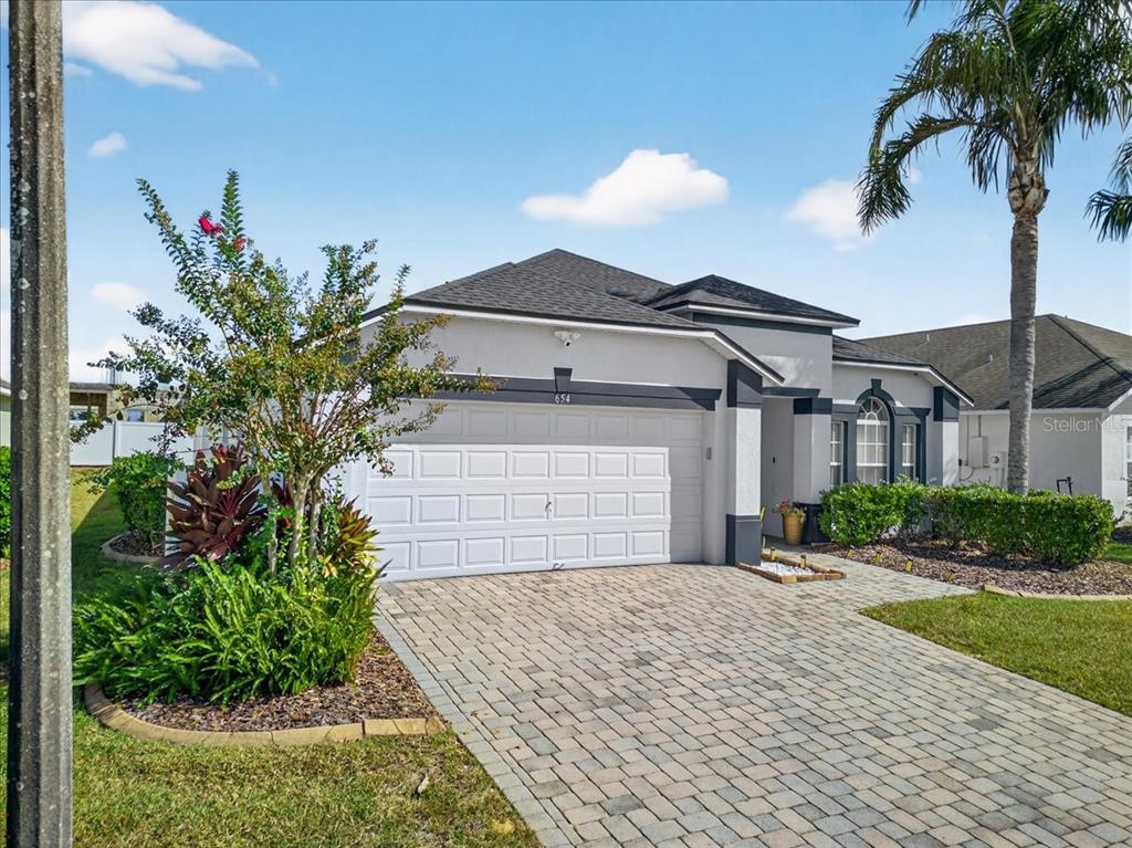 A single-story house with a white garage, gray stucco exterior, and a paved driveway — 654 KILDRUMMY DRIVE, DAVENPORT, FL