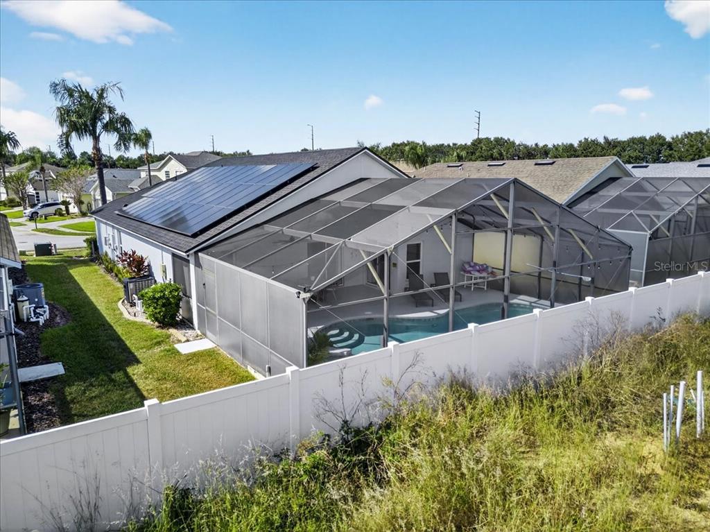 An aerial view of a house with solar panels, a screened-in pool, and a white fence — 654 KILDRUMMY DRIVE, DAVENPORT, FL