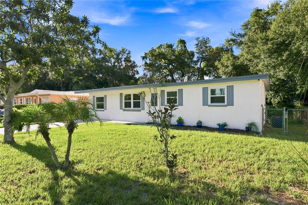 A white single-story house with blue shutters sits on a grassy lot with palm trees — 1120 6TH STREET N, SAFETY HARBOR, FL