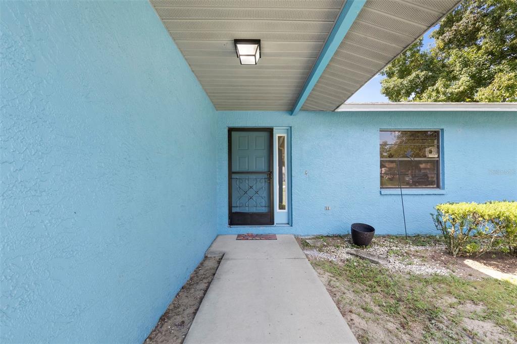 A concrete walkway leads to the front door of a house with bright blue stucco walls — 37216 ORANGE BLOSSOM LANE, DADE CITY, FL