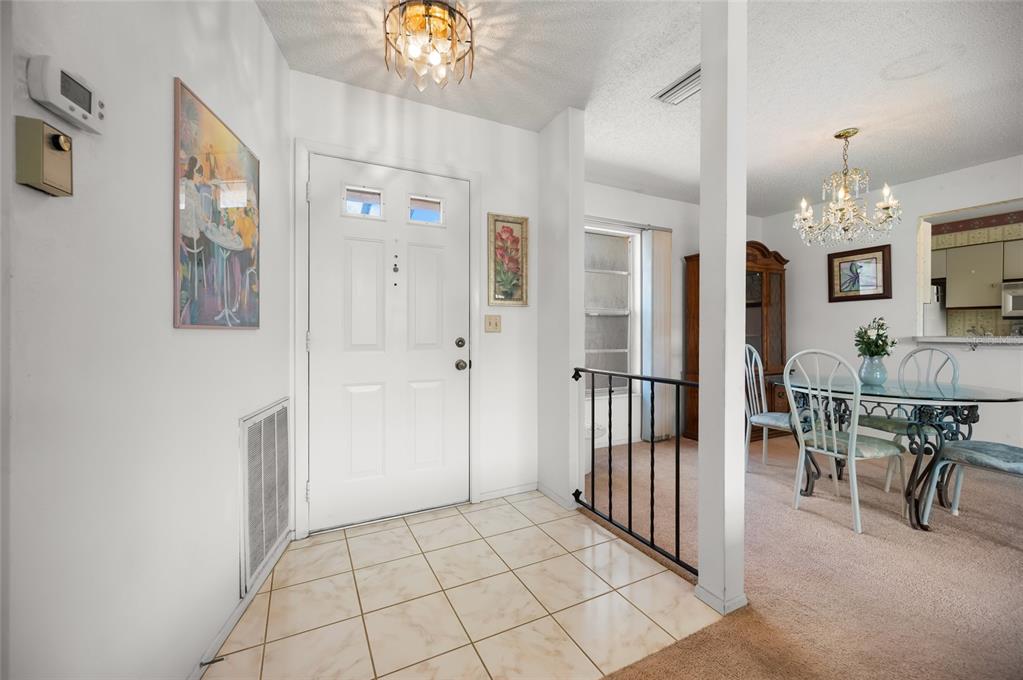 An entryway with tiled floors leads to a dining area with carpet and a chandelier — 658 FOXWOOD BOULEVARD UNIT 88, ENGLEWOOD, FL