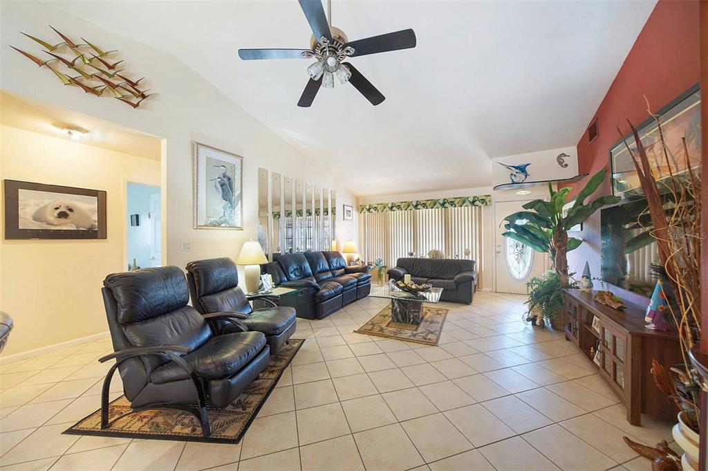 A living room features tile floors, black leather furniture, a ceiling fan, and vaulted ceilings — 901 SW 51ST TERRACE, CAPE CORAL, FL