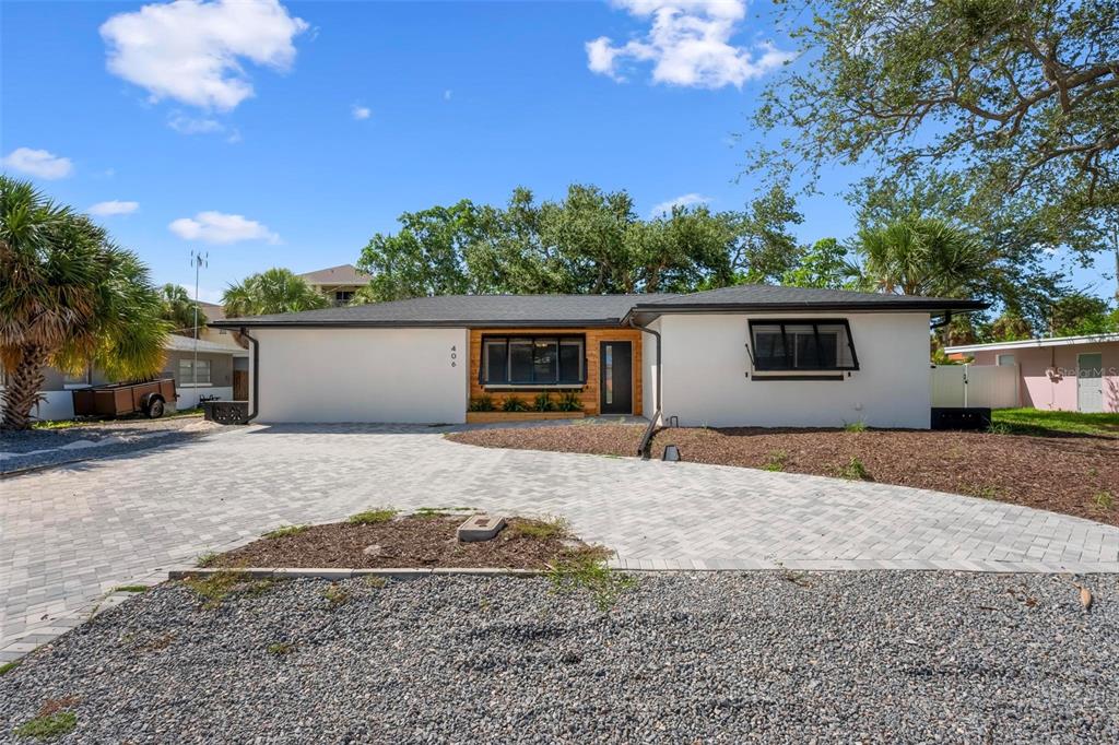 A single-story house with white stucco walls, a wood-accented entryway, and a paved driveway — 406 88TH AVENUE, ST PETE BEACH, FL