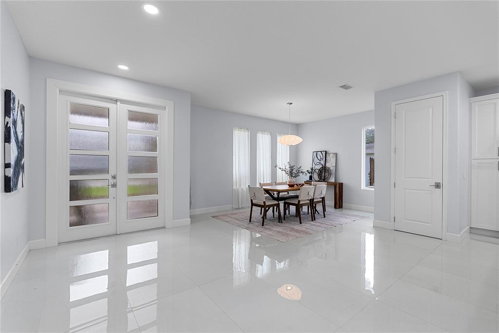 A bright dining area with white tile floors, a wooden table, and double entry doors — 1404 BORDER DRIVE, WINTER PARK, FL