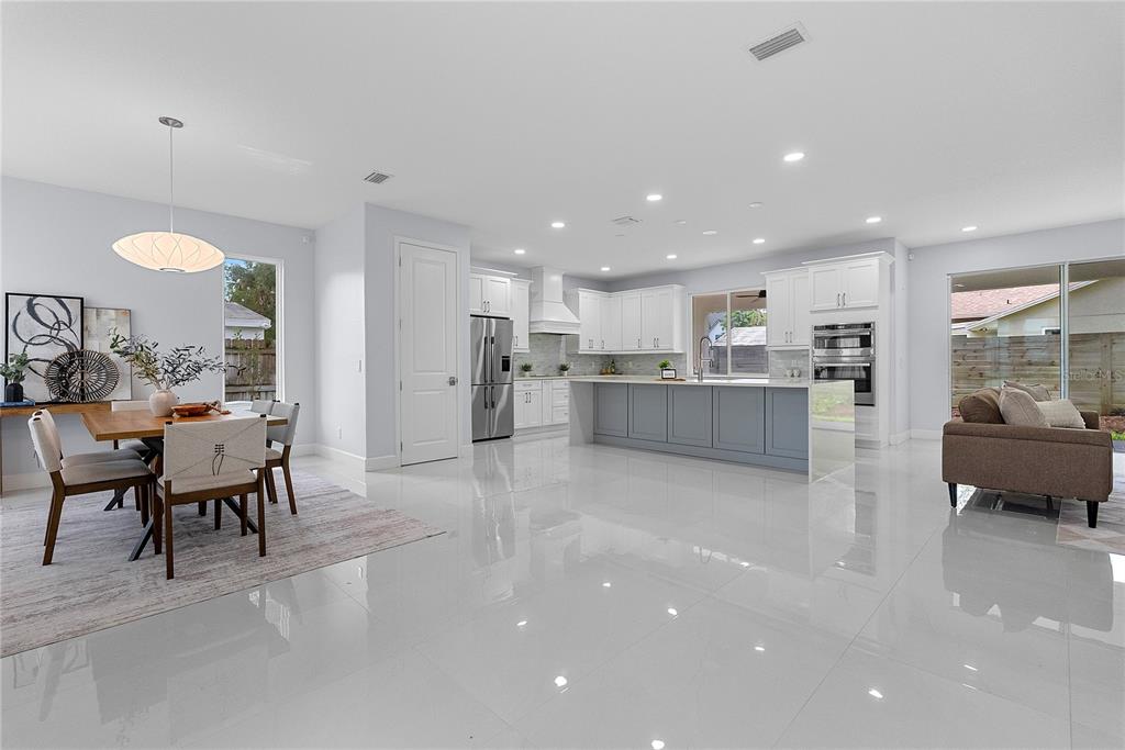 A bright, open-concept kitchen and dining area features white cabinetry, a gray island, and tile flooring — 1404 BORDER DRIVE, WINTER PARK, FL