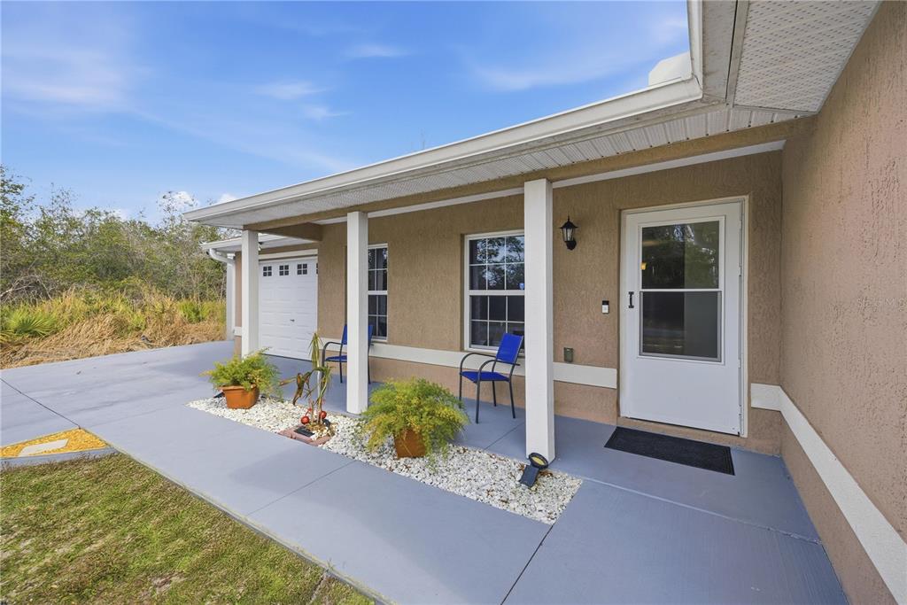 A tan stucco house features a covered front porch with a white door and chairs — 157 SPRUCE ROAD, OCALA, FL