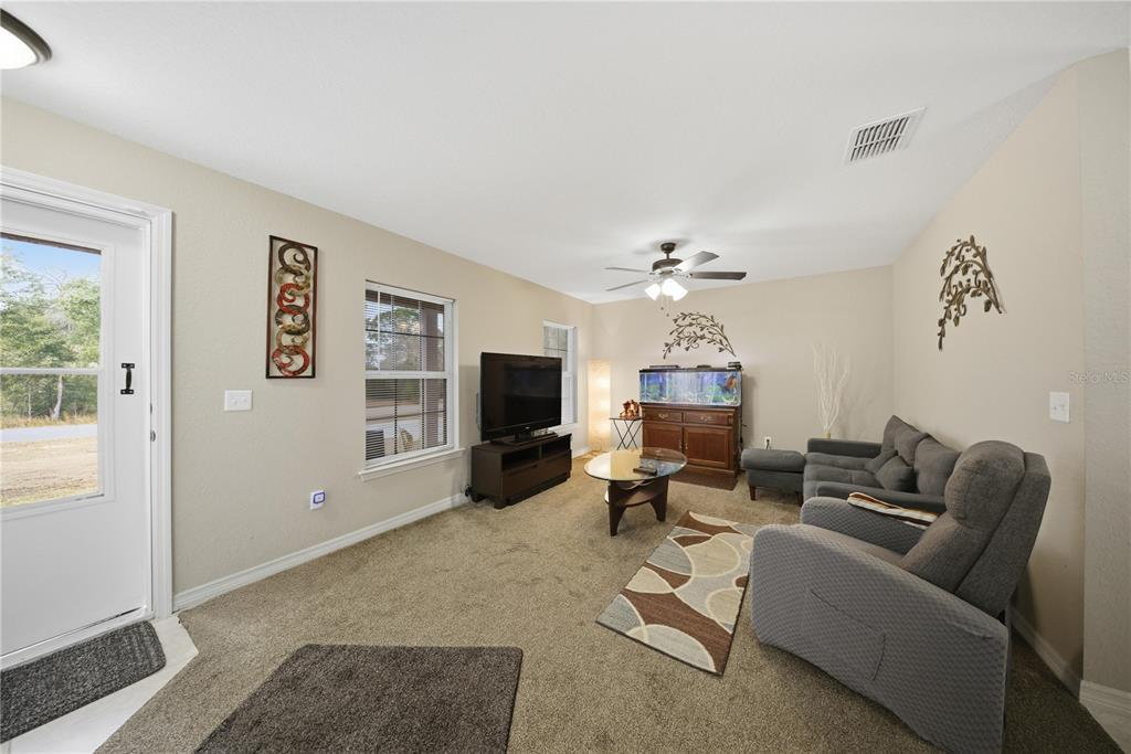 A living room features beige walls, carpeted flooring, a television, a fish tank, and furniture — 157 SPRUCE ROAD, OCALA, FL