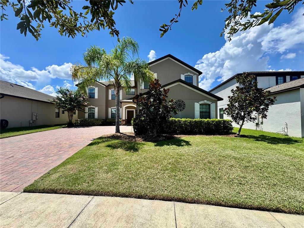 A two-story suburban house with a brick driveway, a palm tree, and a manicured lawn — 2890 SPRING BREEZE WAY, KISSIMMEE, FL