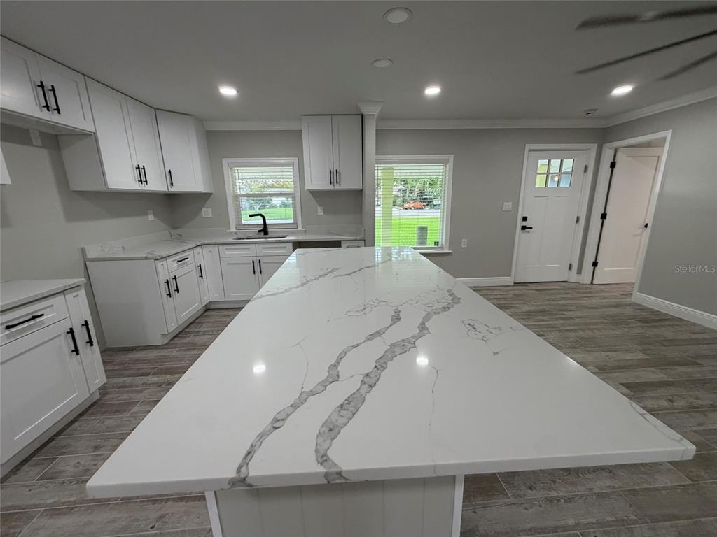 A kitchen features white cabinets, a large marble-patterned island, and light wood-look tile flooring — 8715 DRIFTWOOD DRIVE, TAMPA, FL