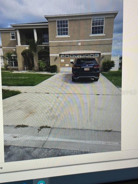 A two-story tan house with a concrete driveway and a dark SUV parked in the garage — 5418 CALLA LILY COURT, KISSIMMEE, FL