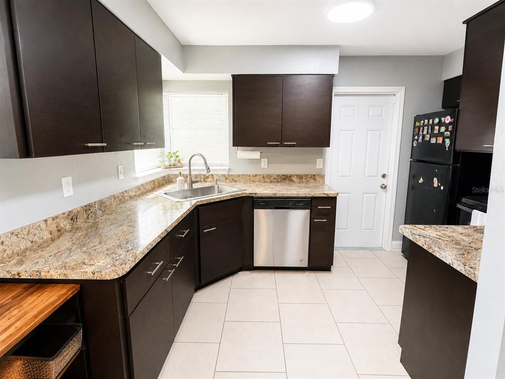 A kitchen features dark wood cabinets, granite countertops, stainless steel appliances, and light tile flooring — 1035 COBBLESTONE AVENUE, DELTONA, FL