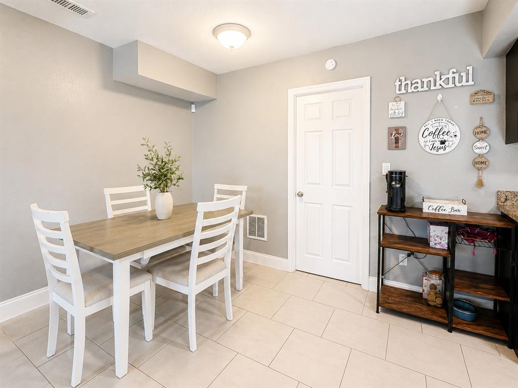A dining area features a wooden table with white chairs, tile flooring, and a coffee station — 1035 COBBLESTONE AVENUE, DELTONA, FL
