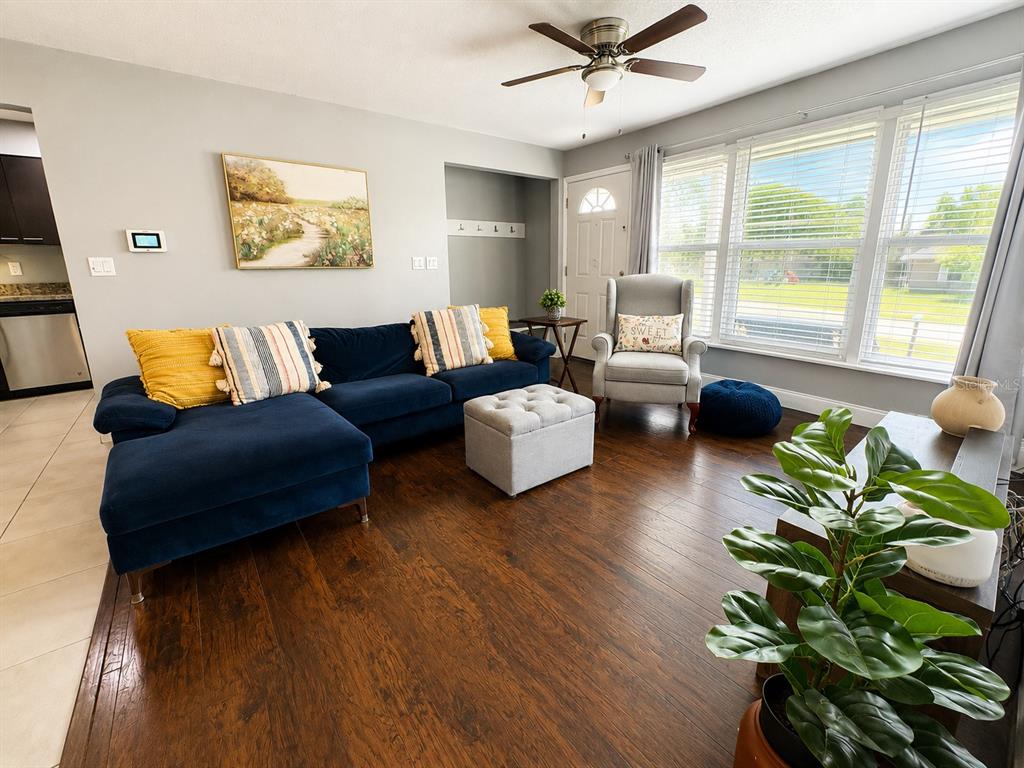 A living room features a blue sectional sofa, a gray armchair, and dark wood flooring — 1035 COBBLESTONE AVENUE, DELTONA, FL