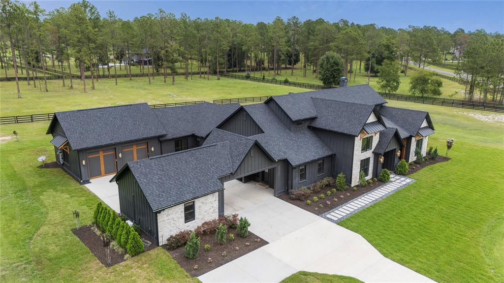 An aerial view of a modern farmhouse with black vertical siding and stone accents — 23741 RIDGE LINK ROAD, EUSTIS, FL