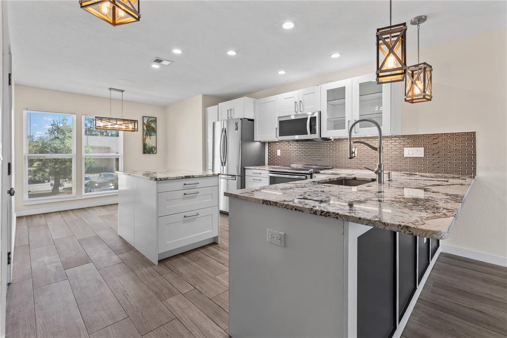 A kitchen features white cabinets, stainless steel appliances, a granite-topped island, and wood-look tile flooring — 3405 CLARK ROAD UNIT 205, SARASOTA, FL