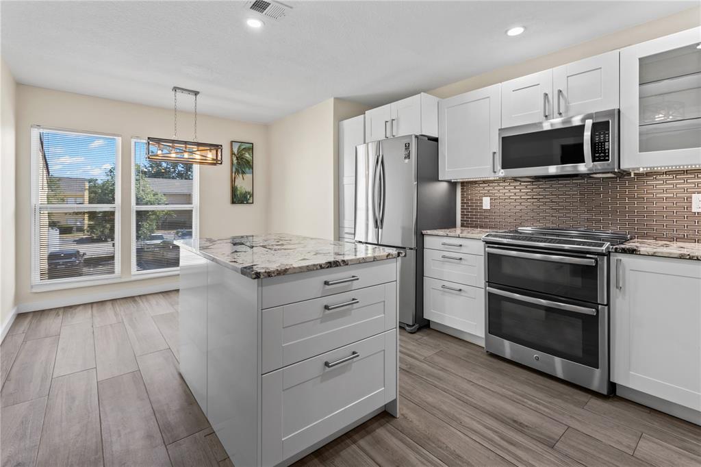 A dining area features wood-look tile flooring, two windows with blinds, and a rectangular light fixture — 3405 CLARK ROAD UNIT 205, SARASOTA, FL