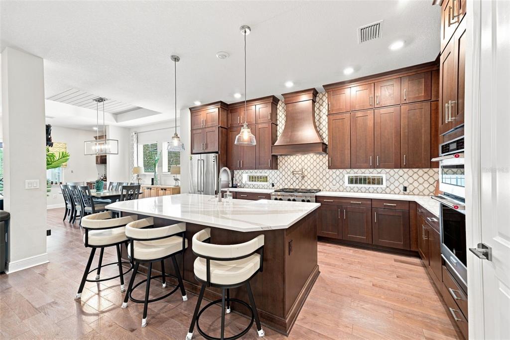 A kitchen features dark wood cabinets, a large white island with stools, and hardwood floors — 4070 EPIC COVE, LAND O LAKES, FL
