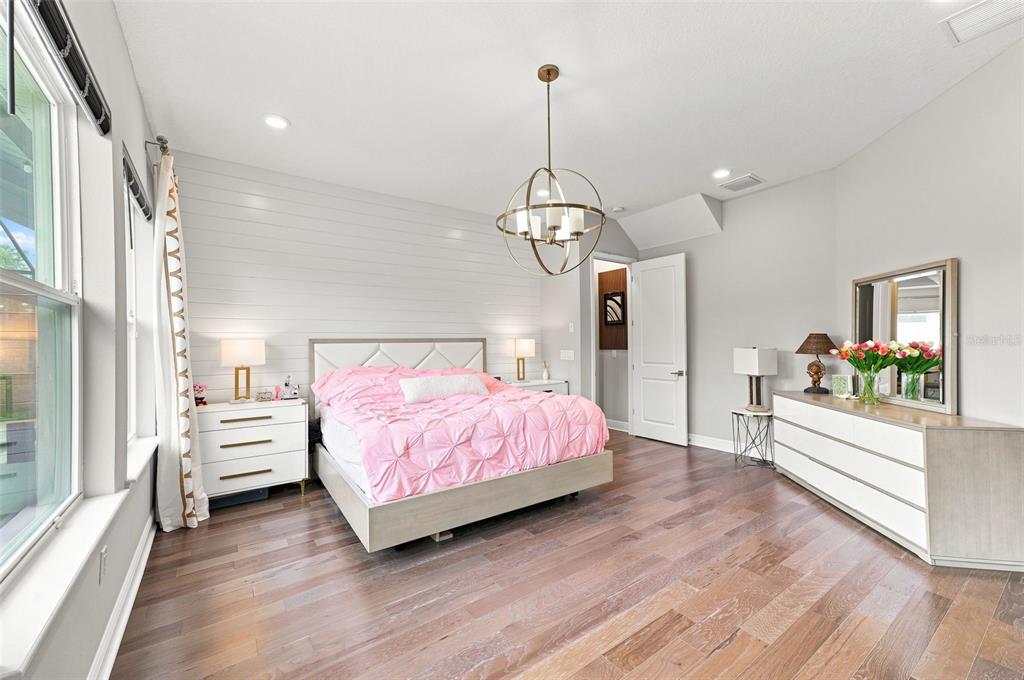 A bedroom features a pink bed, shiplap accent wall, wood flooring, and a globe chandelier — 4070 EPIC COVE, LAND O LAKES, FL