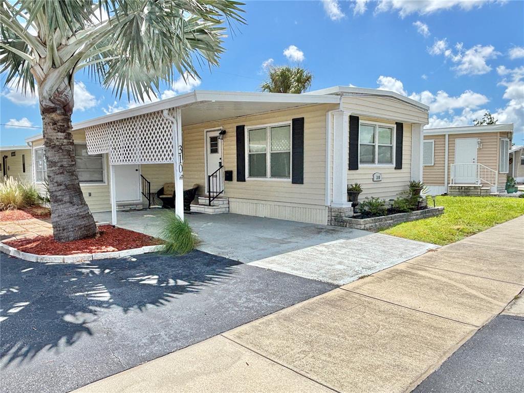 A single-story mobile home with beige siding, black shutters, and a covered carport — 310 MOUNT PINEY AVENUE NE UNIT 266, ST PETERSBURG, FL