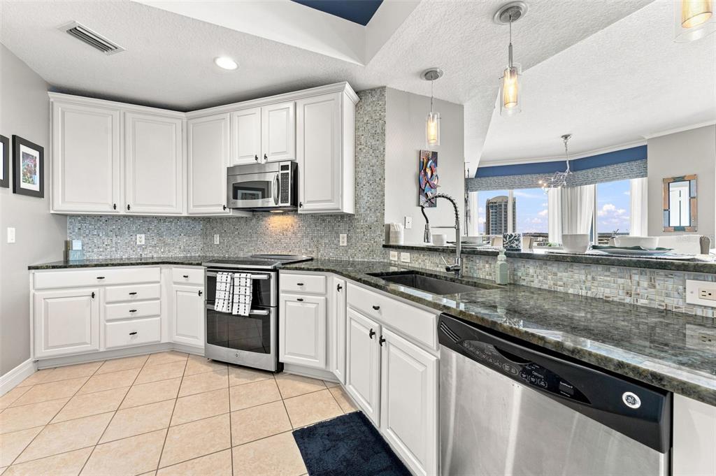 A kitchen features white cabinets, granite countertops, stainless steel appliances, and a tiled backsplash — 1209 E CUMBERLAND AVENUE UNIT 1404, TAMPA, FL