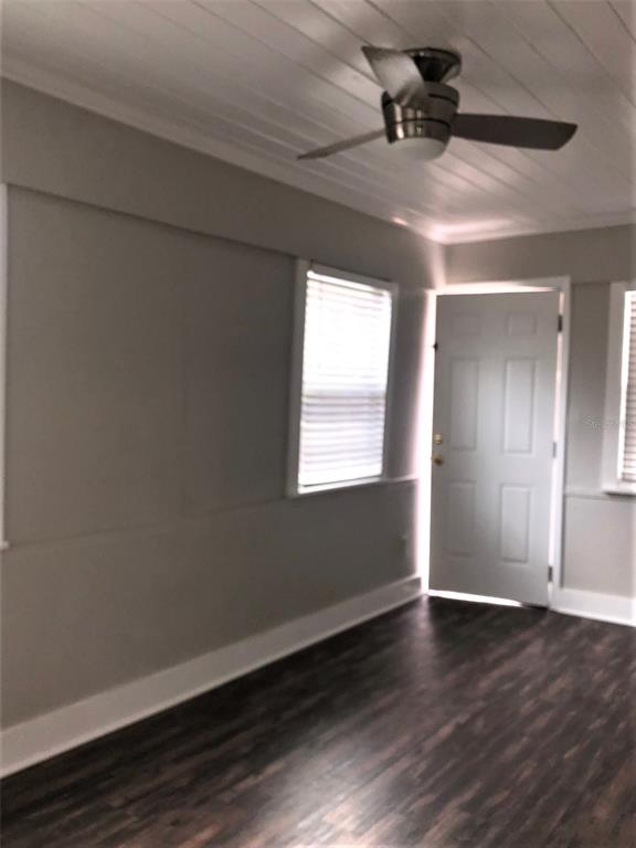 An empty room features dark wood-look flooring, light gray walls, a ceiling fan, and a door — 309 S PARK AVENUE UNIT U, SANFORD, FL