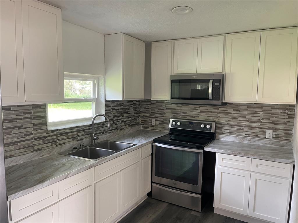A kitchen with white cabinets, stainless steel appliances, marble-look countertops, and a tiled backsplash — 1701 36TH STREET NW, WINTER HAVEN, FL