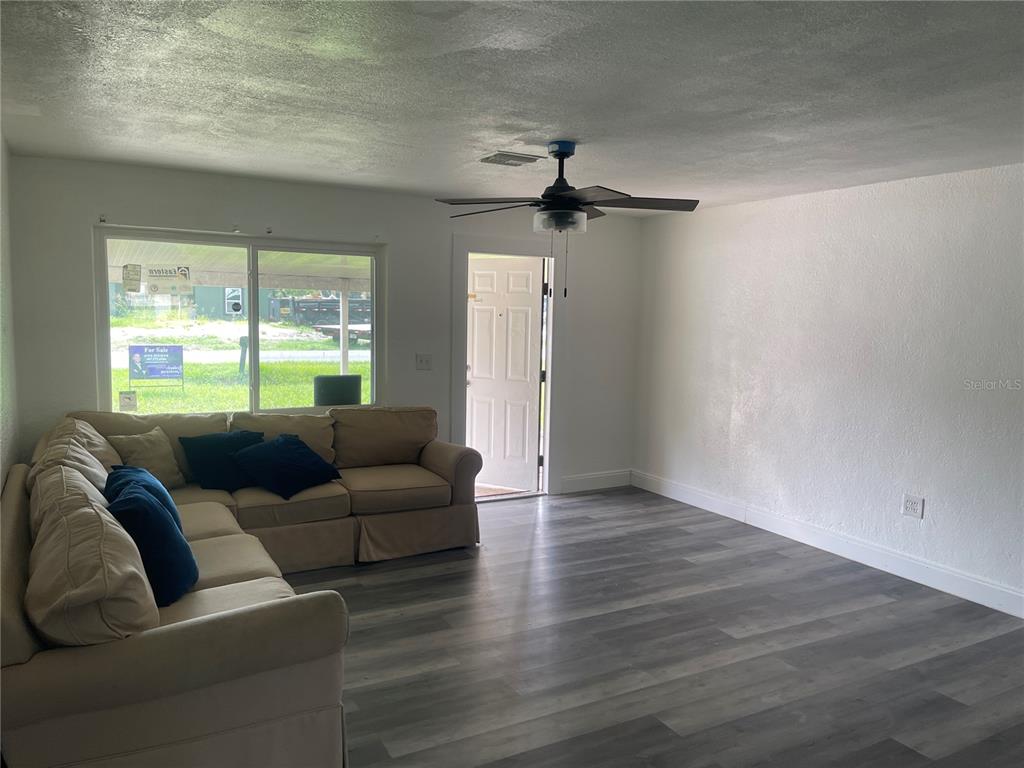 A living room features a beige sectional sofa, gray wood-look flooring, and a ceiling fan — 1701 36TH STREET NW, WINTER HAVEN, FL