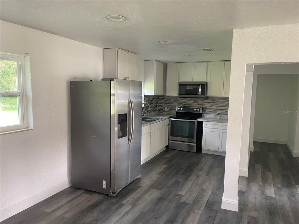 A kitchen features stainless steel appliances, white cabinetry, a tiled backsplash, and wood-look flooring — 1701 36TH STREET NW, WINTER HAVEN, FL