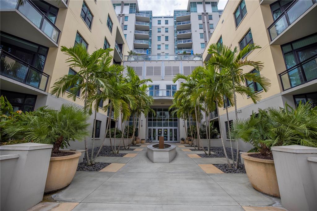 A courtyard with palm trees, a central fountain, and a multi-story apartment building entrance — 400 4TH AVENUE S UNIT 701, ST PETERSBURG, FL
