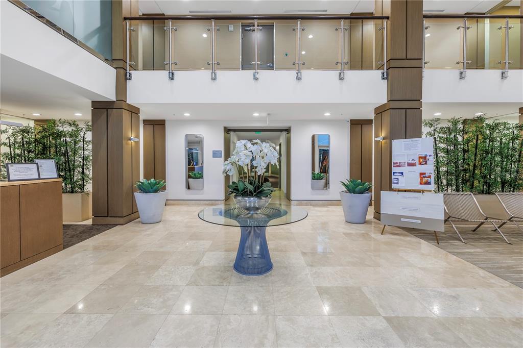 A bright office building lobby features a glass-topped table, potted plants, and marble flooring — 400 4TH AVENUE S UNIT 701, ST PETERSBURG, FL