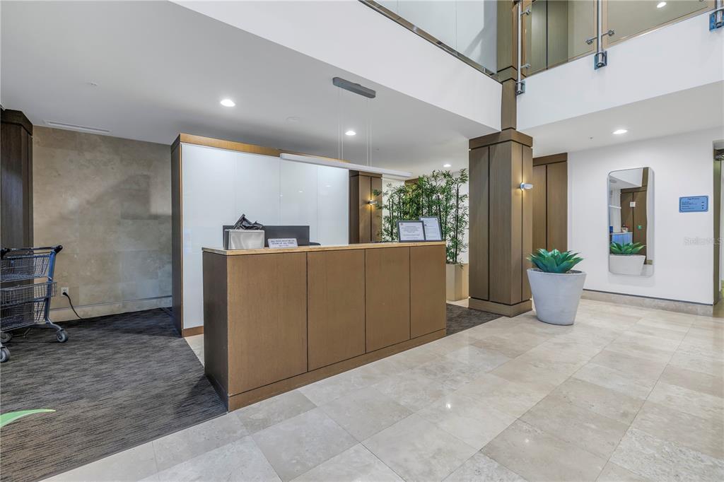 A modern lobby features a wooden reception desk, tile flooring, and a glass-railed mezzanine above — 400 4TH AVENUE S UNIT 701, ST PETERSBURG, FL