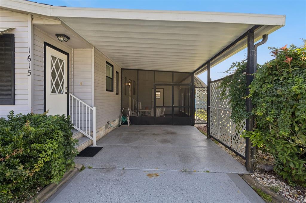 A concrete carport leads to a screened-in porch next to a house with white siding — 1615 PINEHURST DRIVE, LADY LAKE, FL