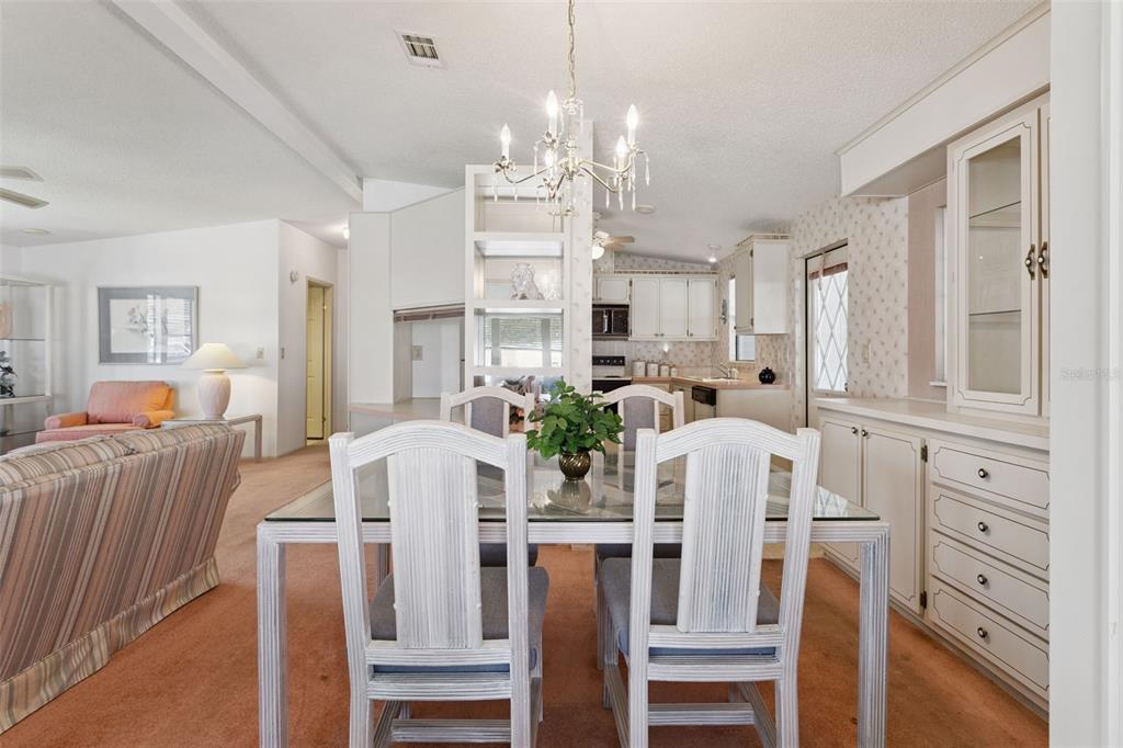 A dining area with a glass table, white chairs, and a chandelier near the kitchen — 1615 PINEHURST DRIVE, LADY LAKE, FL