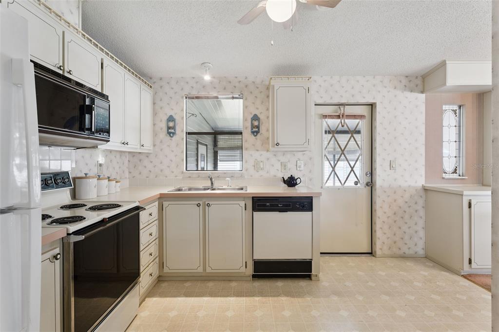 A kitchen features white cabinets, laminate countertops, a black dishwasher, and floral wallpaper — 1615 PINEHURST DRIVE, LADY LAKE, FL