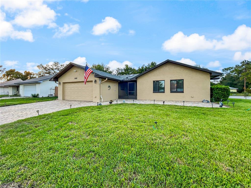 A single-story house with a tan stucco exterior, a paved driveway, and an American flag — 1616 E SANDPIPER TRAIL, CASSELBERRY, FL