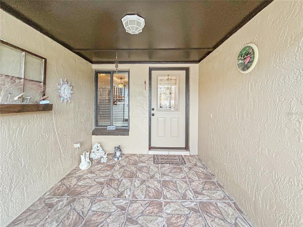 A covered front porch features tiled flooring, a beige door, and a window with blinds — 1616 E SANDPIPER TRAIL, CASSELBERRY, FL
