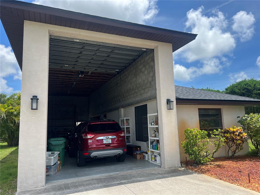 A red SUV is parked inside an open-air garage attached to a residential home — 9438 CRUGAR, ENGLEWOOD, FL