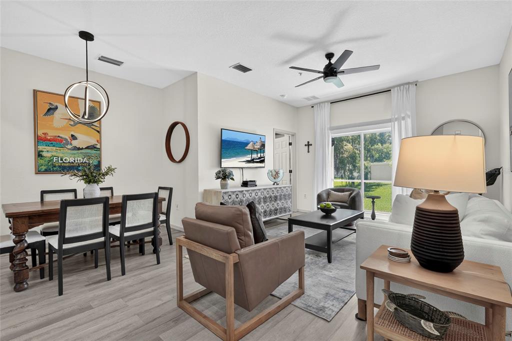 This open-concept living and dining room features light wood flooring, a ceiling fan, and furniture — 3687 PARKRIDGE CIRCLE UNIT 8-106, SARASOTA, FL