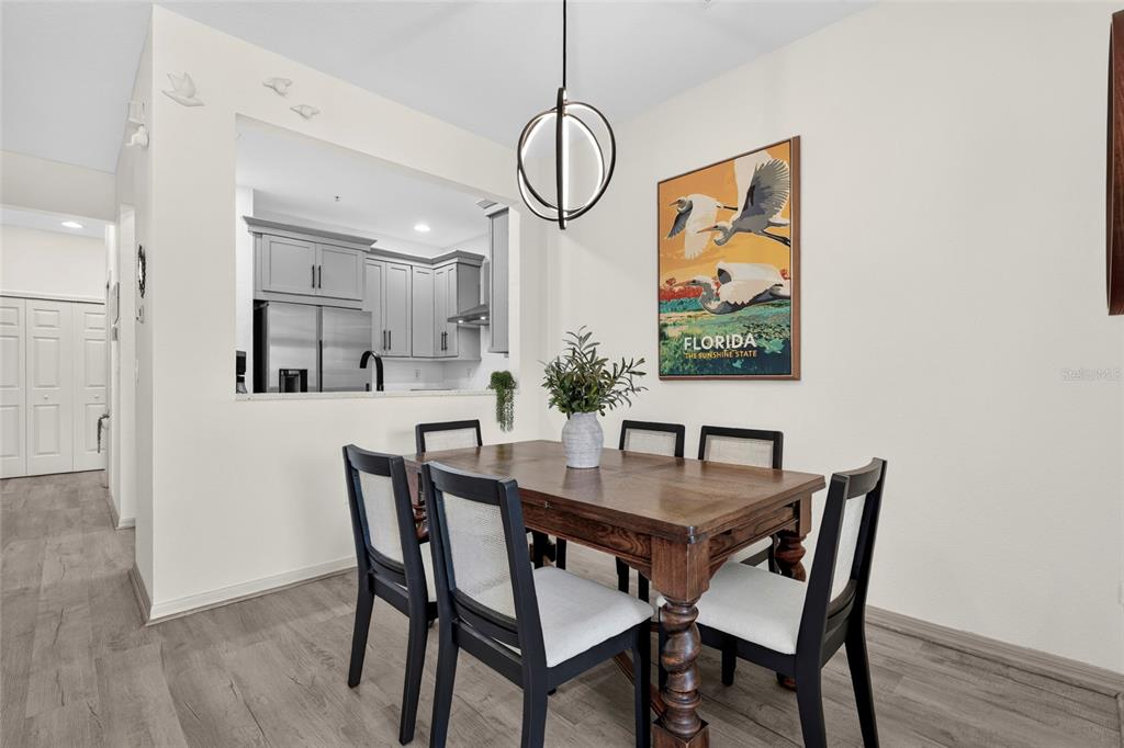 A dining area features a wooden table, four chairs, a modern pendant light, and wall art — 3687 PARKRIDGE CIRCLE UNIT 8-106, SARASOTA, FL