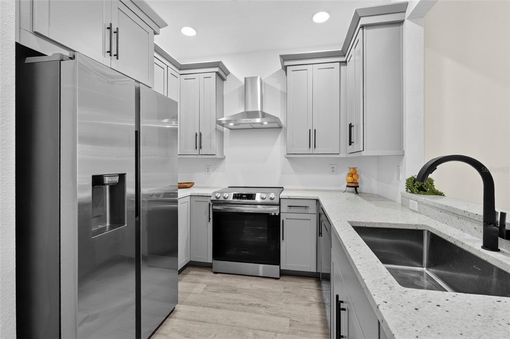 A modern kitchen features gray cabinets, stainless steel appliances, and white speckled countertops — 3687 PARKRIDGE CIRCLE UNIT 8-106, SARASOTA, FL