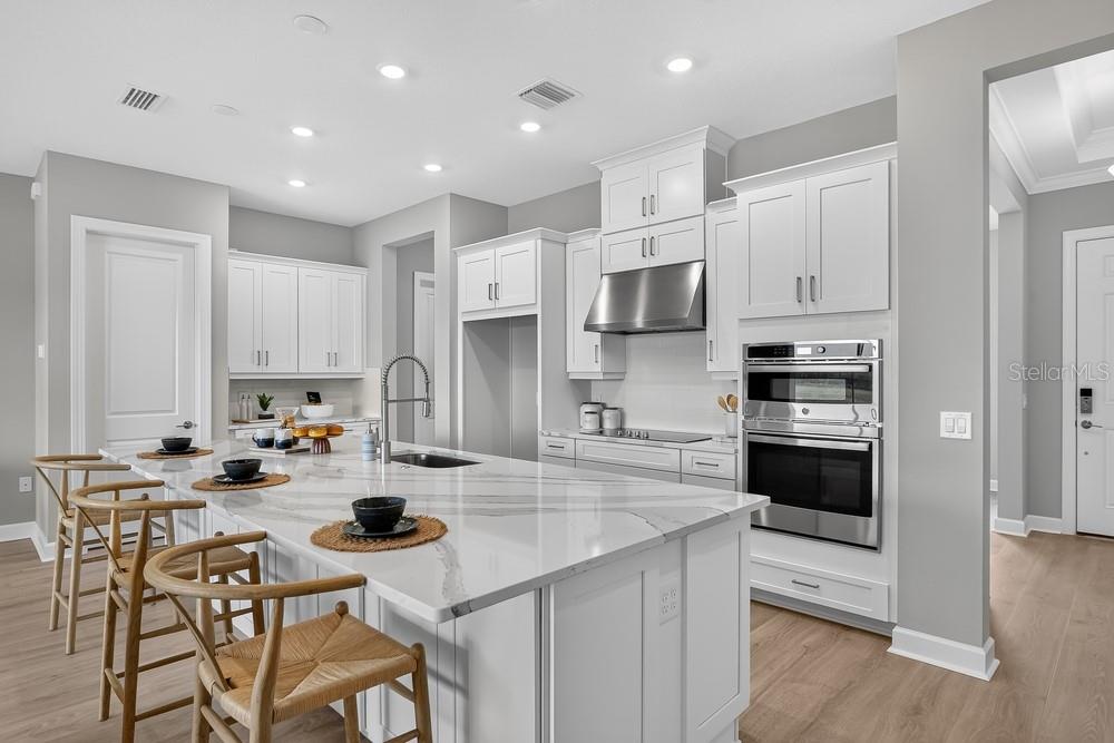 A modern kitchen features white cabinetry, a large marble-topped island, and stainless steel appliances — 5676 NEVIS TERRACE, KISSIMMEE, FL