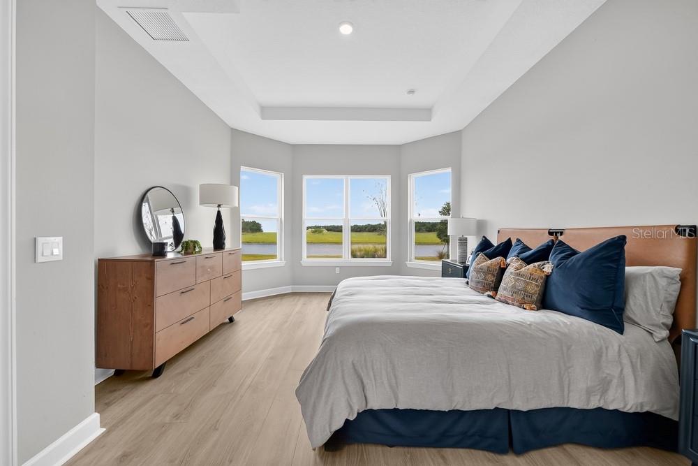 A bedroom features a bed with a textured wall, arched mirrors, and a lake view — 5676 NEVIS TERRACE, KISSIMMEE, FL