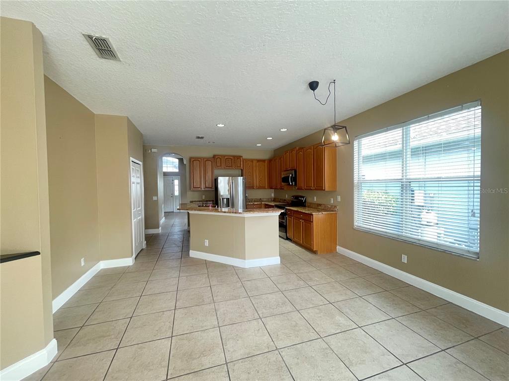 A kitchen with wood cabinets, granite countertops, and tile flooring opens to a dining area — 10366 CYPRESS KNEE CIRCLE, ORLANDO, FL