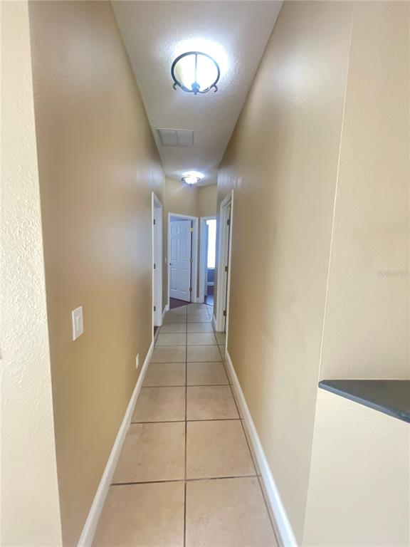 A narrow hallway with tan walls, tiled flooring, and two ceiling light fixtures — 10366 CYPRESS KNEE CIRCLE, ORLANDO, FL