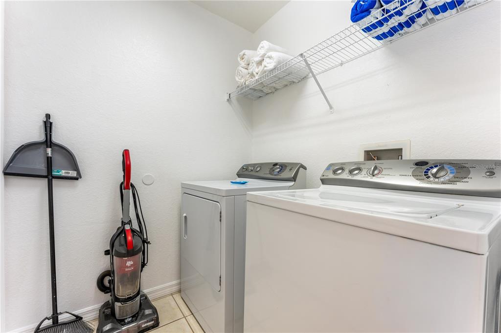 A laundry room featuring a white washer and dryer, a vacuum, and wire shelving — 437 CADIZ LOOP, DAVENPORT, FL