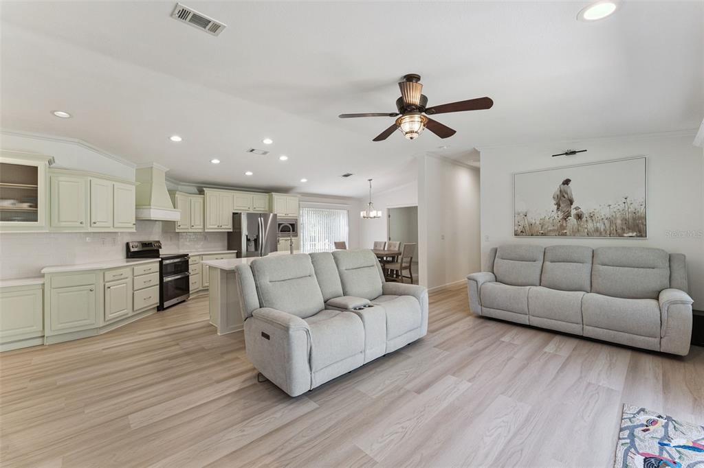 An open-concept living room and kitchen featuring light wood flooring, neutral cabinetry, and two sofas — 1161 LAKE HARNEY WOODS BOULEVARD, MIMS, FL