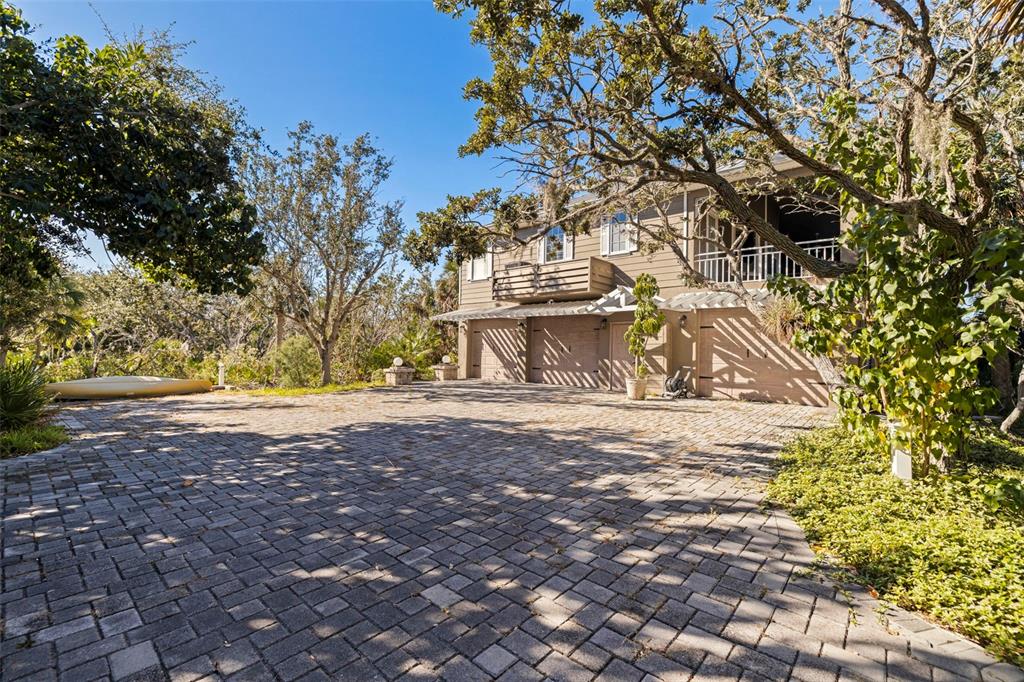 A two-story house with a paved driveway, garage doors, and a balcony surrounded by trees — 2000 BAYVIEW DRIVE, TIERRA VERDE, FL