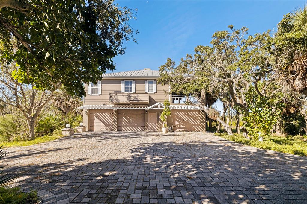 A two-story house with a paved driveway, garage doors, and a balcony surrounded by trees — 2000 BAYVIEW DRIVE, TIERRA VERDE, FL